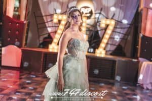 Elegante donna in abito da sera in discoteca 747 Disco, decorazioni luminose e atmosfera festosa.